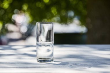 Güneşli bir günde şeffaf bardakta temiz su, ahşap masada.