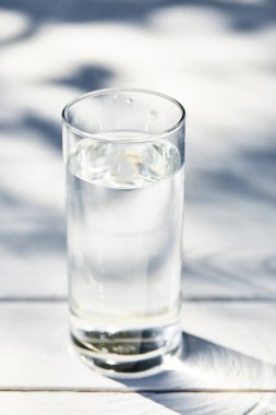 Güneşli bir günde beyaz ahşap masada şeffaf bardakta temiz su.
