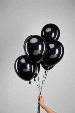 Gri, siyah cuma konsepti üzerinde izole edilmiş siyah balon demetini tutan kadını kısmen görmek