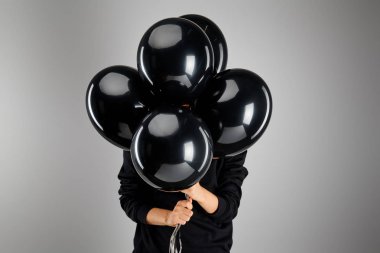 Yüzünün önünde siyah balon tutan bir kadın. Gri, siyah cuma konseptiyle izole edilmiş.