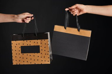 Siyah, siyah cuma konseptiyle izole edilmiş kağıt alışveriş torbaları tutan kadın ve adamın kısmi görüntüsü