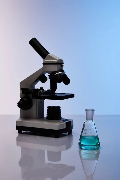 显微镜附近装有彩色蓝色液体的玻璃瓶 — 图库照片
