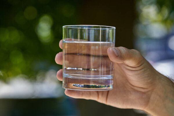 partial view of man holding glass with clear fresh water outdoor