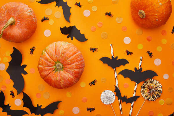top view of pumpkin, bats and spiders with confetti on orange background, Halloween decoration