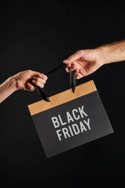 黒で隔絶された黒い金曜日のレタリングで女性と男性のショッピングバッグを保持のクロップドビュー — ストック写真