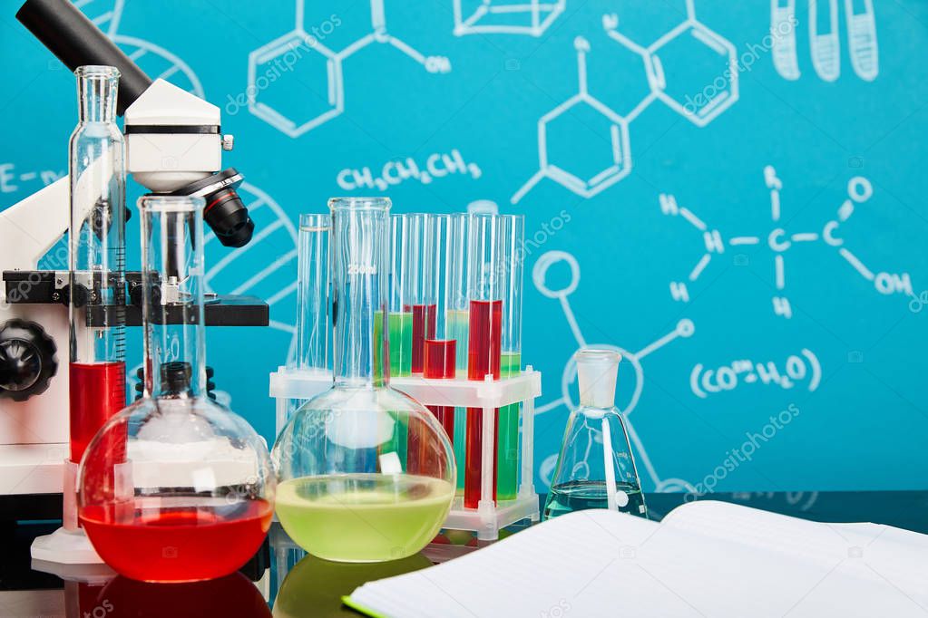 microscope, glass test tubes and flasks with colorful liquid near open copybook on blue background with molecular structure