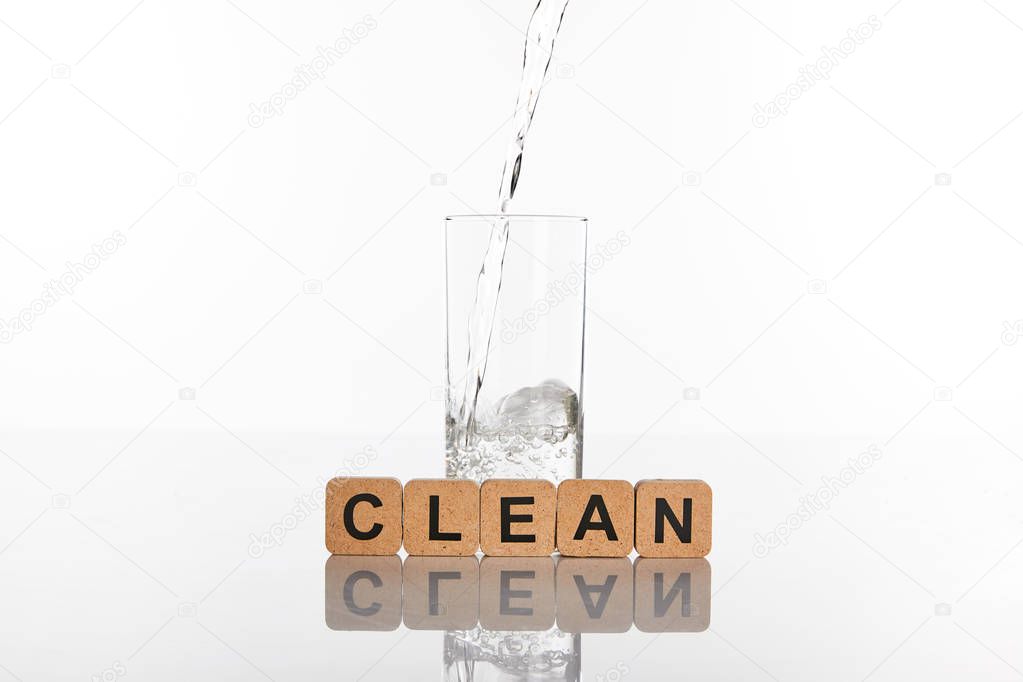 clear fresh water pouring in glass near cubes with clean lettering isolated on white