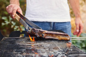 ořezaný pohled na muže s pinzetou grilující maso na grilu 