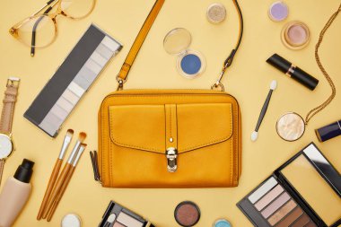 Dekoratif kozmetik ürünleri ve sarı üzerine izole edilmiş kolye yanında çanta manzarası. 