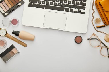 Sarı çantanın yanındaki dizüstü bilgisayarın üst görüntüsü ve gri üzerine izole edilmiş dekoratif kozmetik ürünler. 