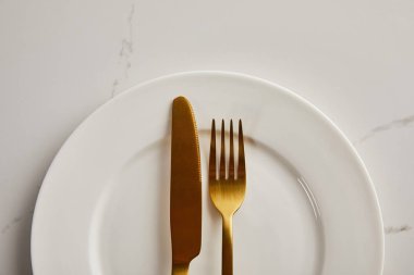 Altın bıçak ve çatalın üst görüntüsü mermer masada temiz beyaz tabak üzerinde