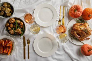 top view of served thanksgiving dinner with grilled turkey, whole pumpkins and baked vegetables on white tablecloth clipart