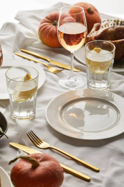 Gül şarabı, limon suyu, çatal bıçak takımı ve balkabağı ile servis edilen beyaz masa örtüsü.
