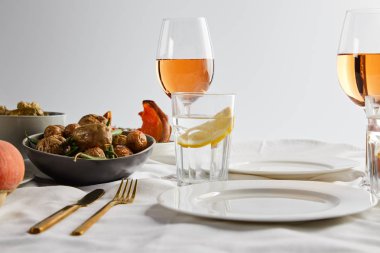 Gül şarabı ve limonlu bardakların yanında fırında patates ve gri masa örtüsünün üzerinde limon suyu.
