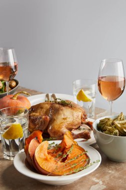 sliced baked pumpkin near grilled turkey and glasses with rose wine on stone table isolated on grey clipart