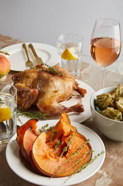grilled whole turkey near baked sliced pumpkin and bowl with physalis near glasses with rose wine and lemon water isolated on grey clipart