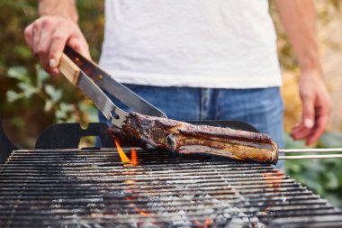 Kırpılmış cımbızla adam barbekü ızgarasında et pişiriyor. 