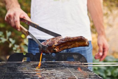 cropped view of man with tweezers grilling meat on barbecue grid  clipart