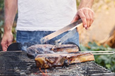 Kırpılmış cımbızla adam barbekü ızgarasında et pişiriyor. 