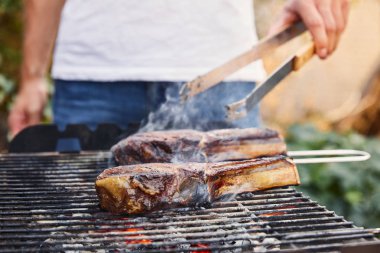 Kırpılmış cımbızla adam barbekü ızgarasında et pişiriyor. 