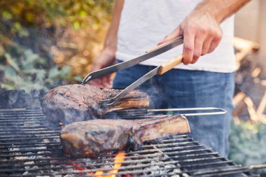 cropped view of man with tweezers grilling meat on barbecue grid  clipart