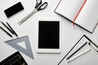 Pano, not defteri, kalemler, makas, üçgen cetvel, hesap makinesi, akıllı telefon ve dijital tabletin üst görünümü 