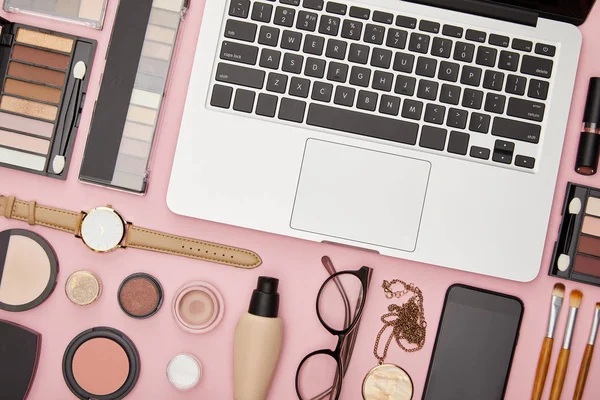 笔记本电脑的顶视图 靠近装饰化妆品和用粉色隔离的眼镜 — 图库照片