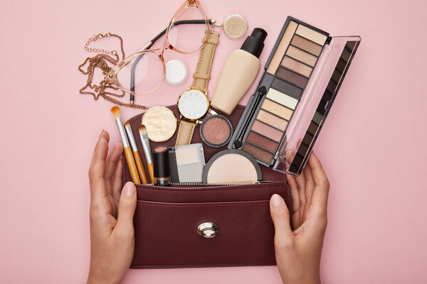 top view of woman near bag with decorative cosmetics isolated on pink 