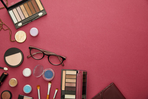 top view of decorative cosmetics near glasses and necklace on crimson 