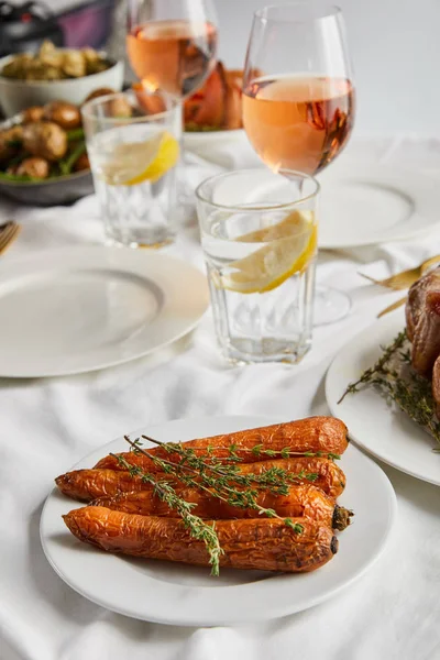 烤胡萝卜 迷迭香近眼镜 玫瑰酒和柠檬水在白色桌布上 — 图库照片
