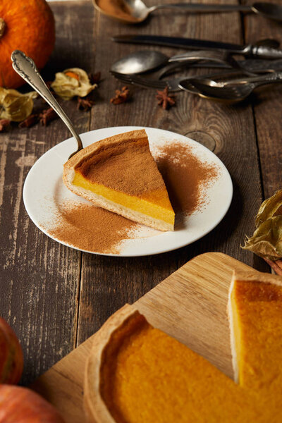 delicious pumpkin pie with cinnamon powder near cutlery on dark wooden surface