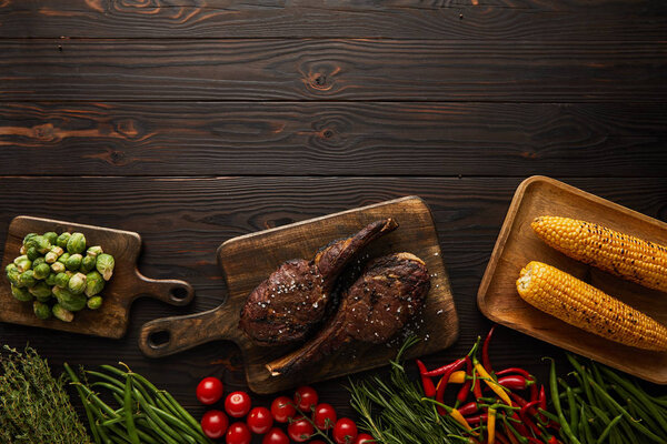 вид сверху на мясо, кукурузу, перец чили, помидоры черри, зеленый горох, зелень, брюссельскую капусту на разделочной доске
 