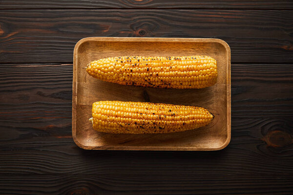 top view of tasty and organic corn on wooden plate 