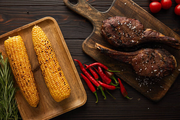 top view of meat, corn, chili peppers, cherry tomatoes, greenery