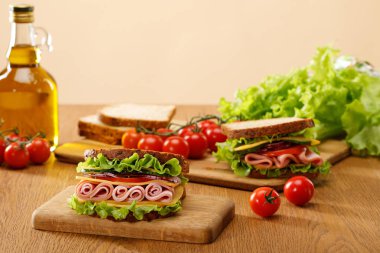 Marul, ekmek, kiraz domatesleri ve bej üzerine izole edilmiş ahşap masa üzerindeki yağın yanında taze sandviçin seçici odağı.