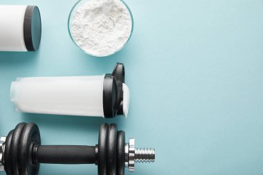 Spor şişesinin yanındaki dambıl ve mavi üzerine protein tozu. 