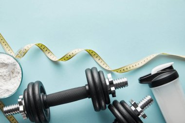 Spor şişesinin üstünde mavi halterlerin yanında protein içeceği var. 