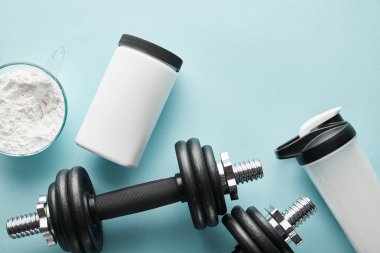 top view of dumbbells near sports bottle and protein powder on blue  clipart