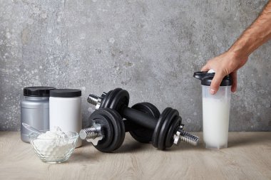 Kırpılmış insan manzarası, beton duvarın yanında protein içeceği ile spor şişesi tutan adam. 