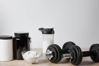 Spor şişesinde protein içeceği, kavanozların yanında ve dambılların üzerinde beyaz 