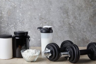 Spor şişesinde protein içeceği ve beton duvarın yanında protein tozu. 