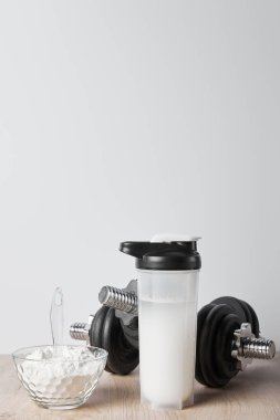 Siyah dambılların yanında protein içeceği ve gri renkli protein içeceği olan cam kase.