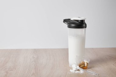 Gri renkte izole edilmiş bademlerin yanında protein içeceği bulunan bir şişe.