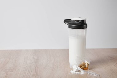 sports bottle with protein shake near almonds isolated on grey clipart