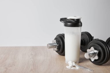 spoon with protein powder near heavy dumbbells and sports bottle isolated on grey clipart