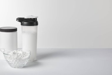 Kavanozun yanında protein içeceği ve beyaz üzerinde protein tozu olan spor şişesi. 