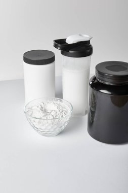 jars and sports bottle with protein shake near bowl with protein powder on white  clipart