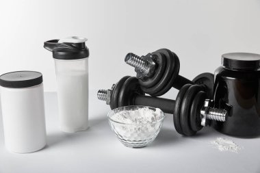 jars and sports bottle near bowl with protein powder and dumbbells on white  clipart