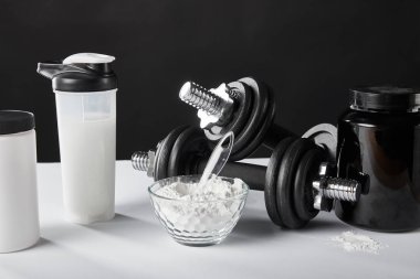 Spor şişesinin yanındaki cam kasede siyah protein içeceği var. 