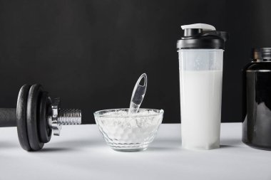 Dambıl ve spor şişesinin yanında siyah protein içeceği. 
